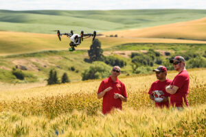 Dr. Arron Carter with students flying a drone in a wheat field