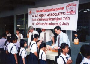 two men at display table hand out sandwiches to children