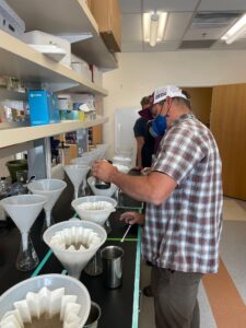 A man pours malt barley wort into funel filters on a research bench. 