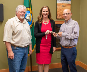 Washington Grain Commission (WGC) Chairman Mike Carstensen, CEO Casey Chumrau, and retiring CEO Glen Squires pose for a photo smiling. 