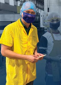 Two men in hairnets and face masks holding crackers
