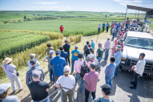 Man in red presents to a crowd of people in a wheat field