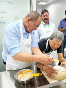 Two men in aprons prepare bread for baking