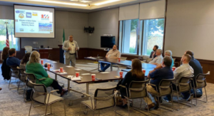 people sit around a table while a man presents. 