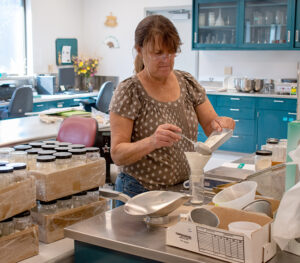 A woman standing at a counter measuring flour into a jar through a funnel. 