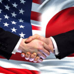 Hands shaking with American and Japanese flags in the background